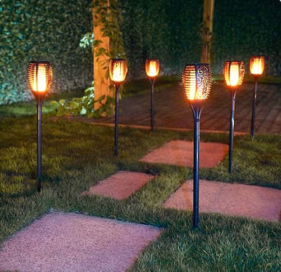 Estaca antorcha solar con efecto llama decorando jardín por la noche