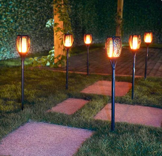 Estaca antorcha solar con efecto llama decorando jardín por la noche